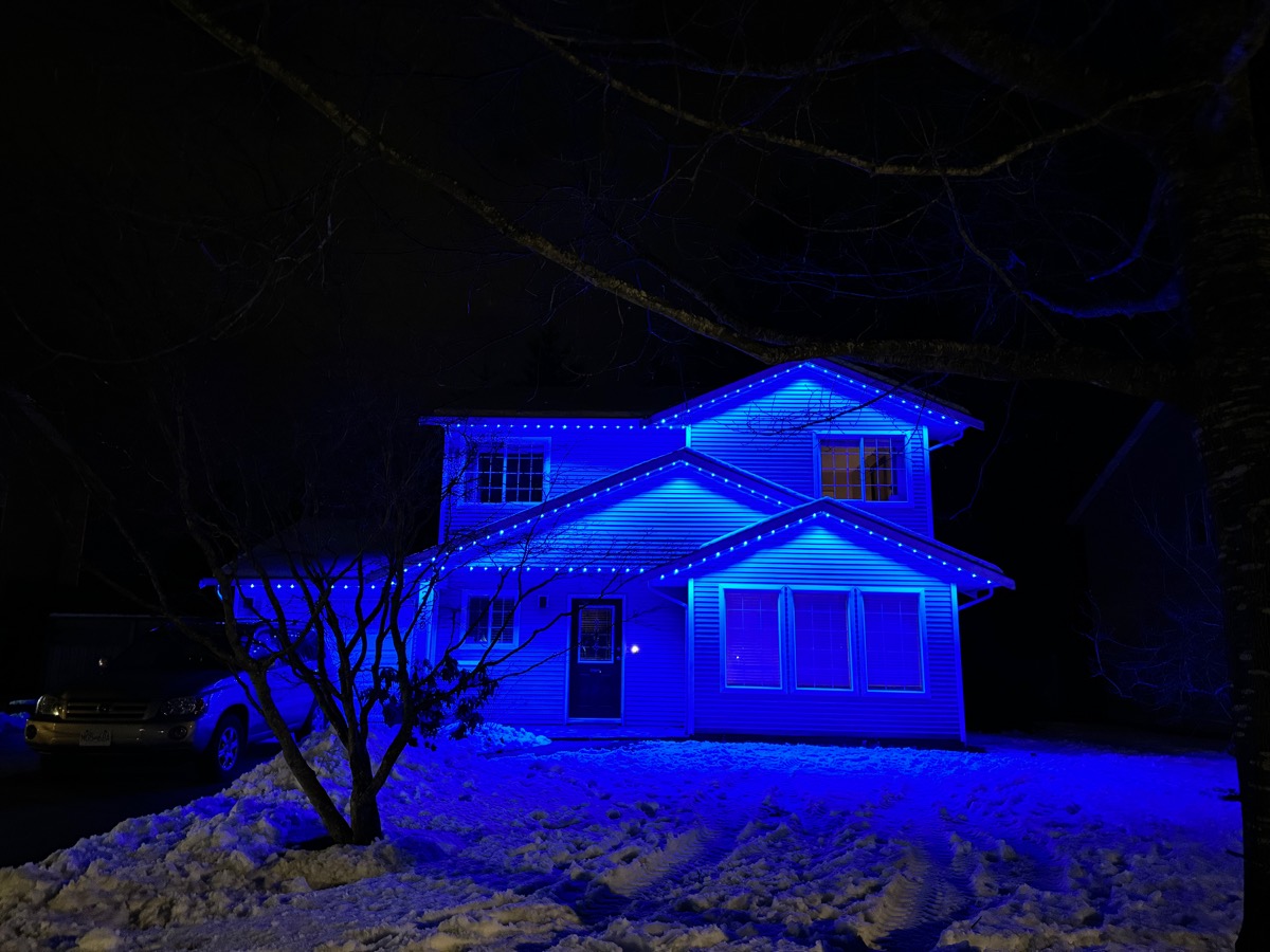 Gemstone Lights washing a two-storey home in blue on a snowy night.