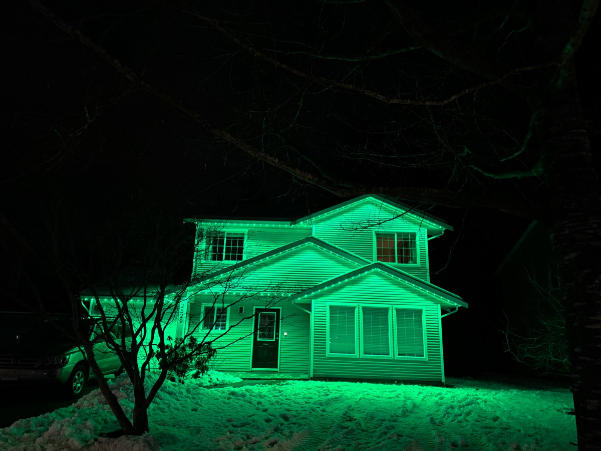A home's rooflines glowing green with Gemstone Lights over fresh snow.