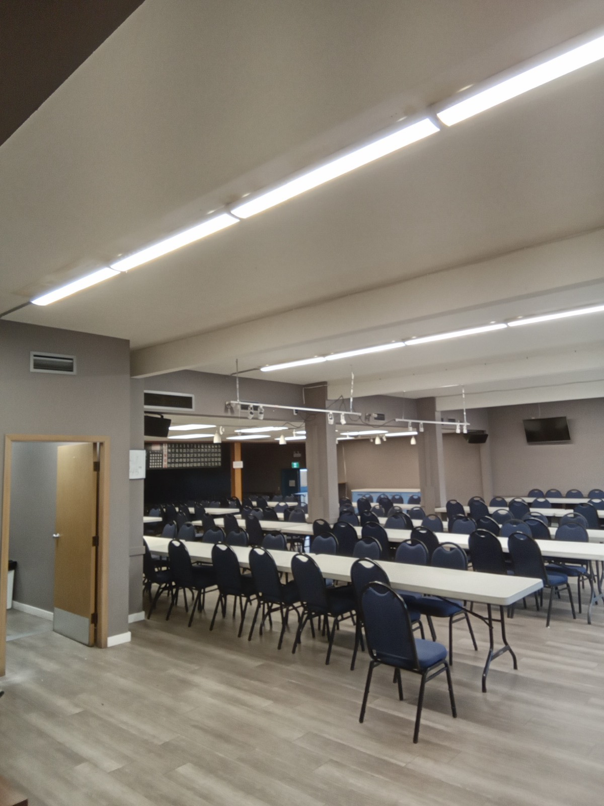 LED batten fixtures over a meeting hall set with rows of chairs.
