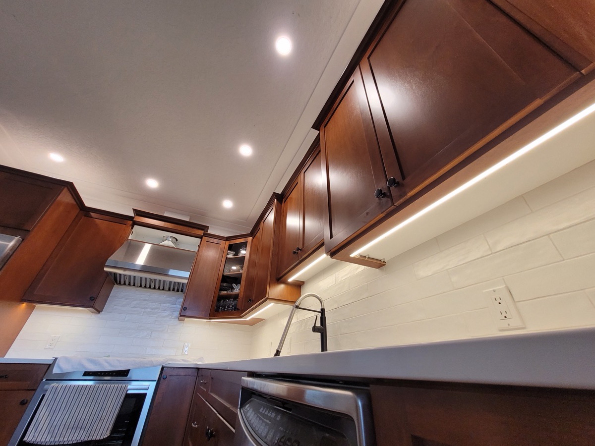 Pot lights and warm under-cabinet lighting in a kitchen with dark wood cabinets.
