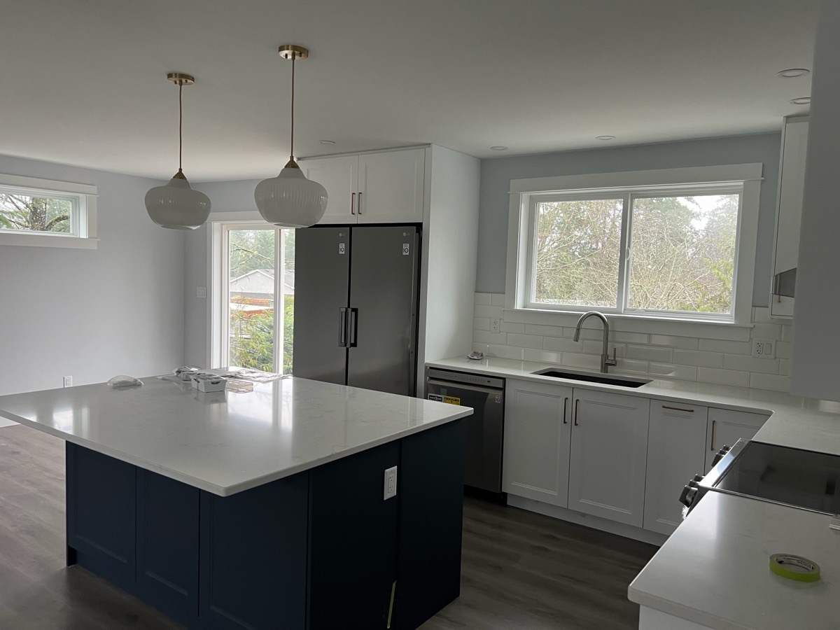 Globe pendants and pot lights over a navy kitchen island in a renovated home.