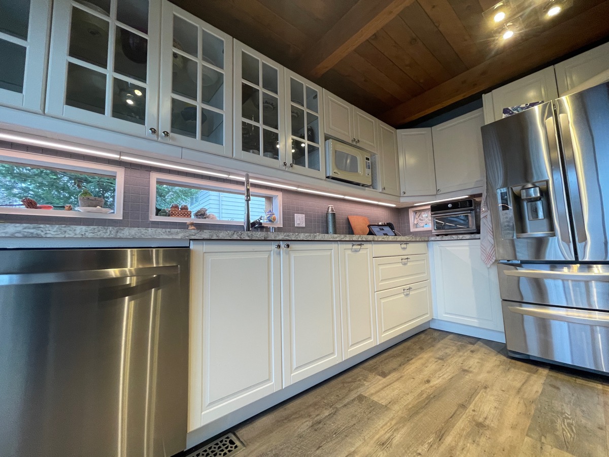 Under-cabinet lighting below glass-front cabinets in a white kitchen.