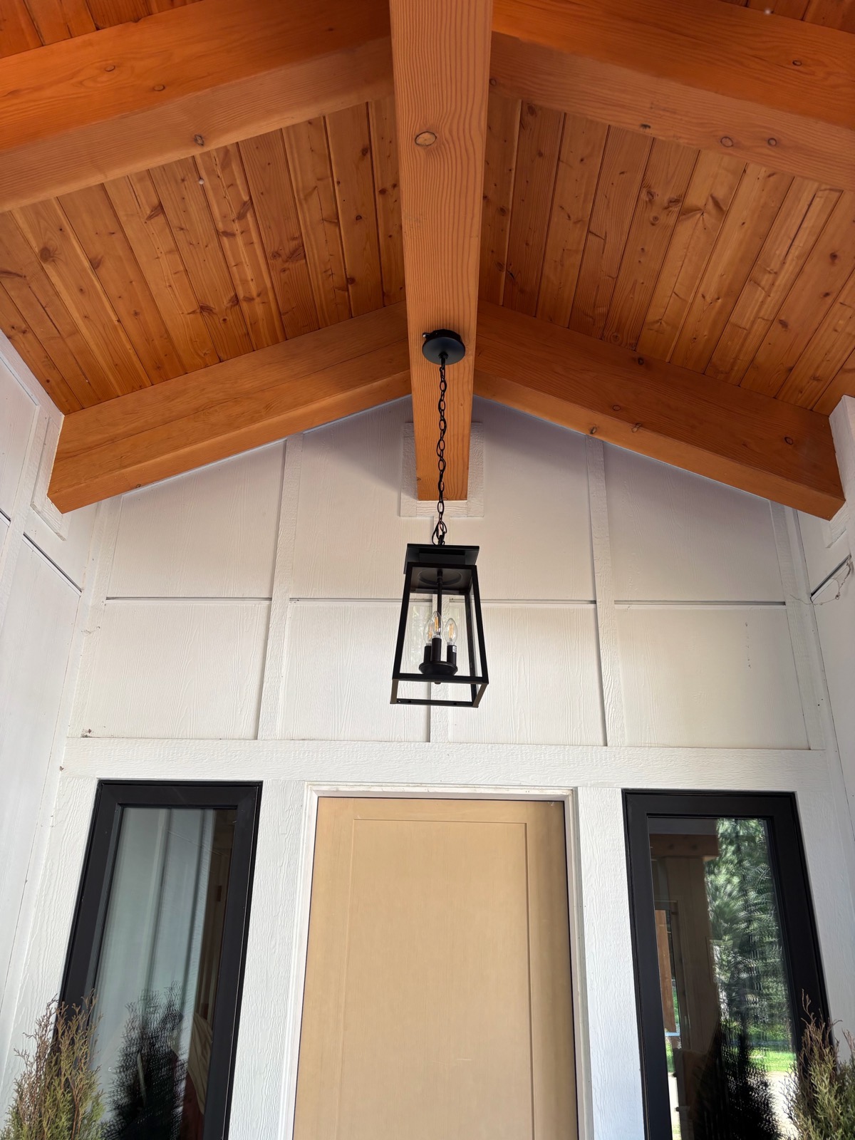 A black lantern pendant in a covered entry with a cedar-plank vaulted ceiling.